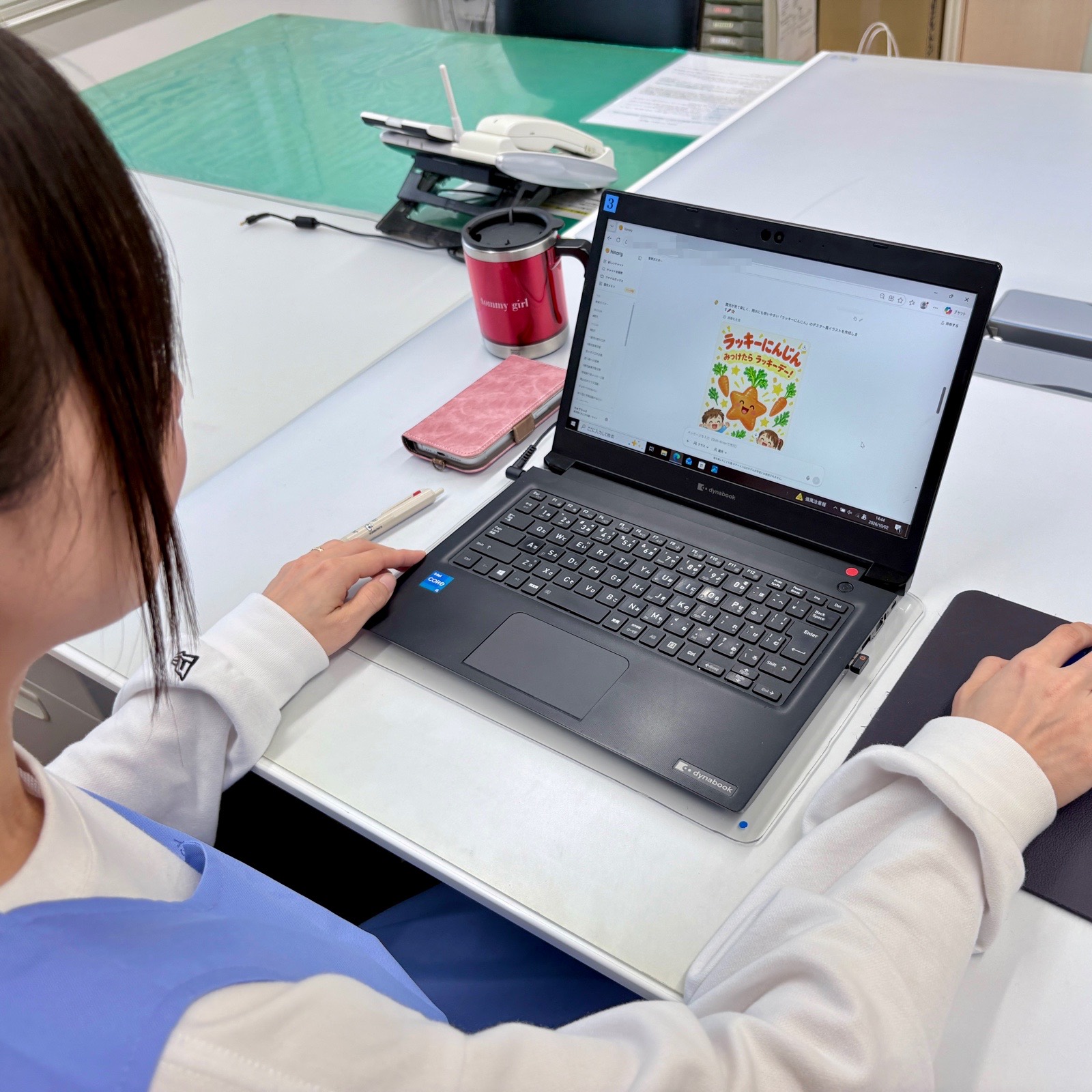 ノートパソコンでヒナリーを操作する先生。画面にヒナリーが作成した掲示物のイラストが表示されている